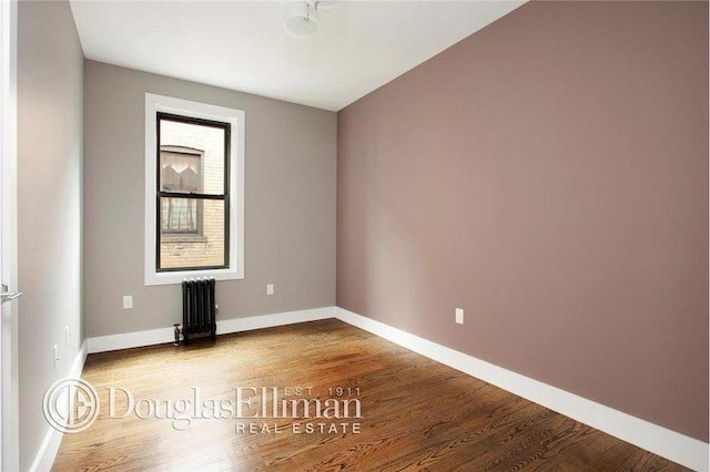 empty room with baseboards, radiator heating unit, and wood finished floors