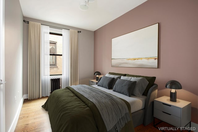 bedroom with radiator heating unit, baseboards, and light wood-style flooring