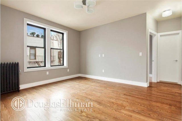 unfurnished room featuring baseboards, light wood-style flooring, and radiator heating unit