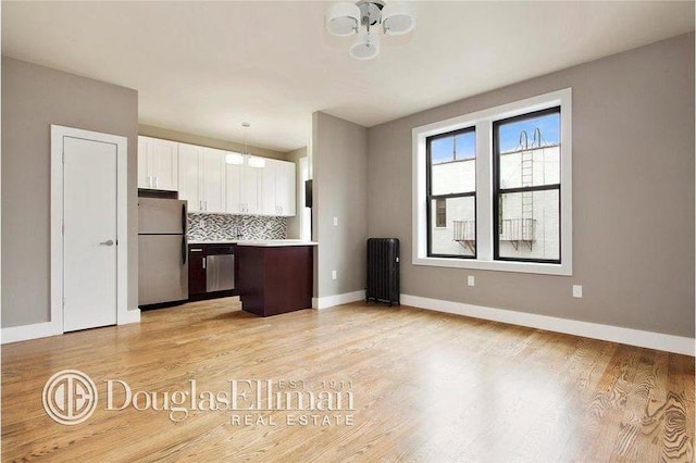 kitchen featuring tasteful backsplash, radiator heating unit, light wood-style flooring, white cabinets, and stainless steel appliances