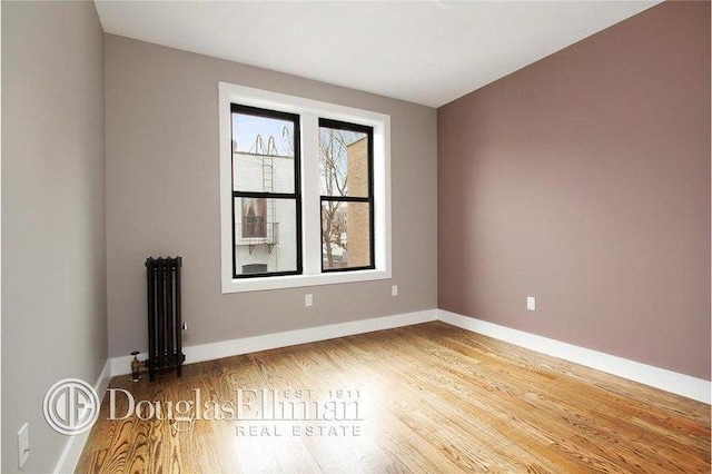 spare room with radiator heating unit, baseboards, and wood finished floors