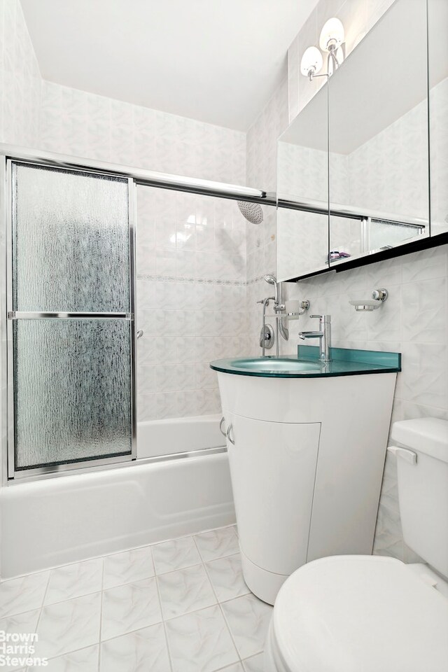 full bath with combined bath / shower with glass door, vanity, toilet, and tile walls