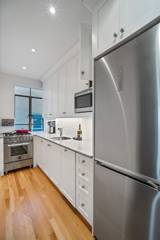 kitchen with a sink, white cabinets, appliances with stainless steel finishes, light stone countertops, and light wood finished floors