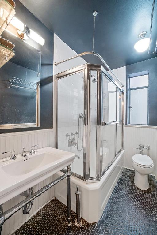 full bathroom with combined bath / shower with glass door, sink, wood walls, and toilet