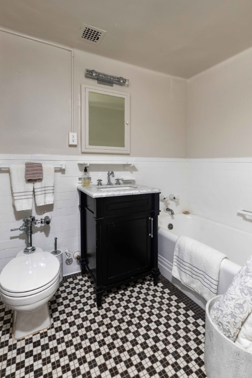 bathroom featuring toilet, tile walls, a tub to relax in, and vanity