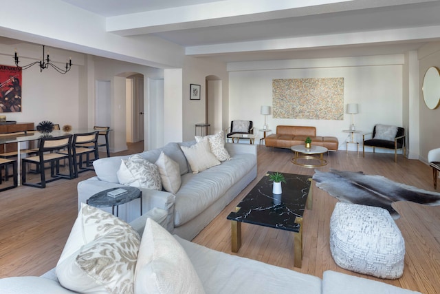 living area featuring arched walkways, a notable chandelier, beamed ceiling, and wood finished floors