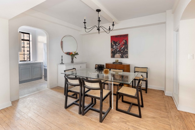 dining area with arched walkways, light wood-type flooring, beam ceiling, and baseboards