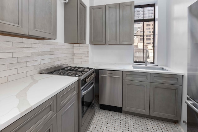 kitchen featuring tasteful backsplash, stainless steel appliances, light stone counters, gray cabinets, and sink