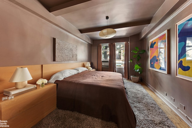 bedroom featuring beam ceiling, wood finished floors, and baseboards