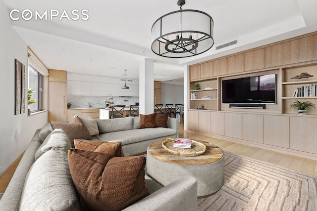 living area featuring a tray ceiling, wood finished floors, visible vents, and an inviting chandelier