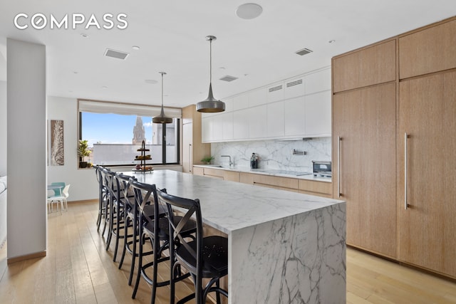 kitchen with light wood-type flooring, a center island, visible vents, and decorative backsplash