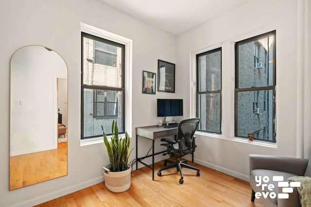 home office featuring arched walkways, baseboards, and wood finished floors