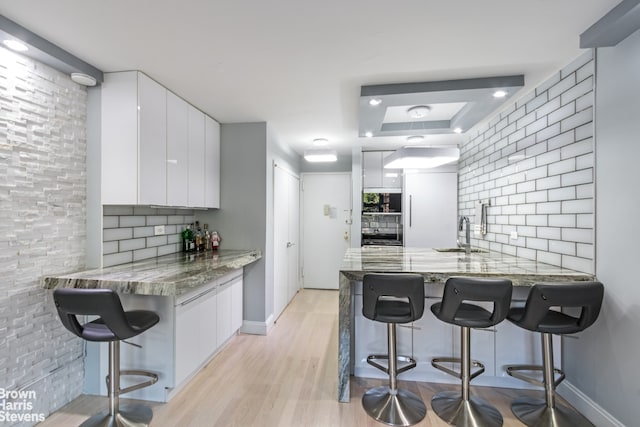 kitchen with modern cabinets, a sink, backsplash, white cabinetry, and a peninsula