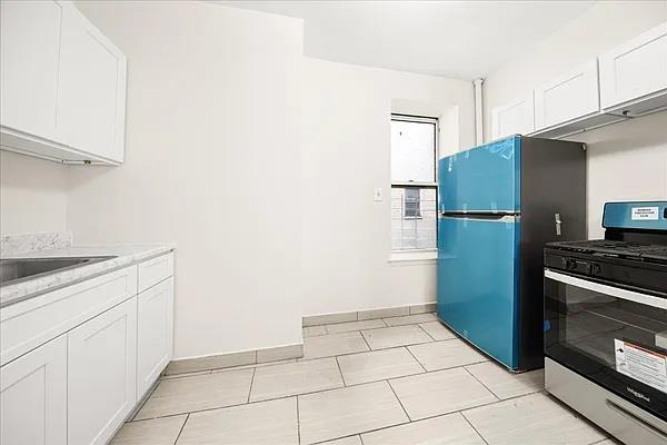 kitchen with light tile patterned floors, stainless steel gas range oven, refrigerator, and white cabinetry