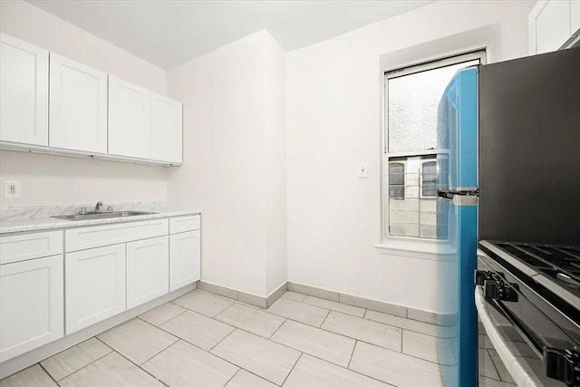 kitchen with light tile patterned floors, white cabinetry, gas range, stainless steel refrigerator, and sink