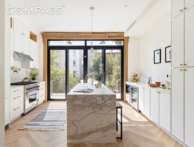 kitchen with high end range, white cabinets, under cabinet range hood, and a sink