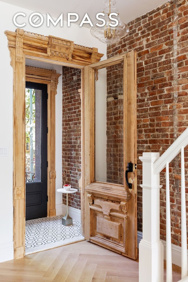 entrance foyer featuring an inviting chandelier, brick wall, stairs, and baseboards