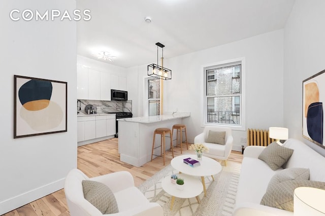 living area featuring an inviting chandelier, light wood-type flooring, radiator heating unit, and baseboards