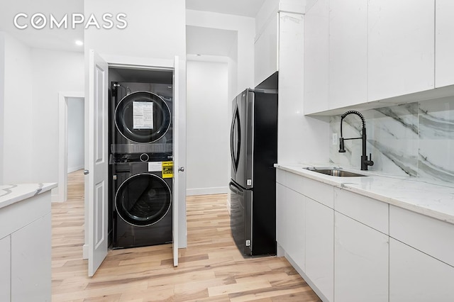 laundry area with laundry area, stacked washer and clothes dryer, light wood-type flooring, and a sink