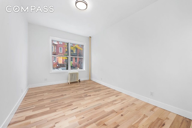 empty room with baseboards, wood finished floors, and radiator heating unit