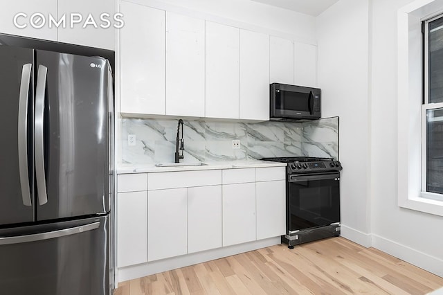 kitchen featuring light wood-type flooring, a sink, tasteful backsplash, freestanding refrigerator, and gas stove