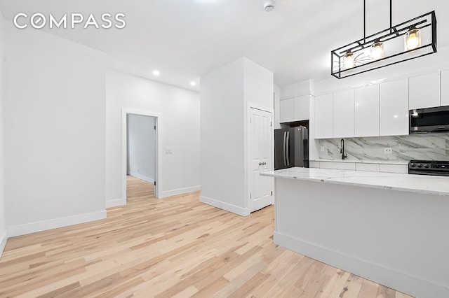 kitchen with light wood finished floors, freestanding refrigerator, black gas range, white cabinets, and stainless steel microwave