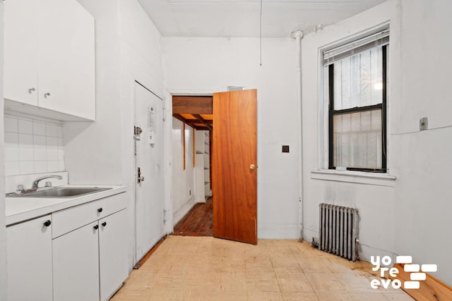 kitchen with radiator, white cabinets, light countertops, and a sink