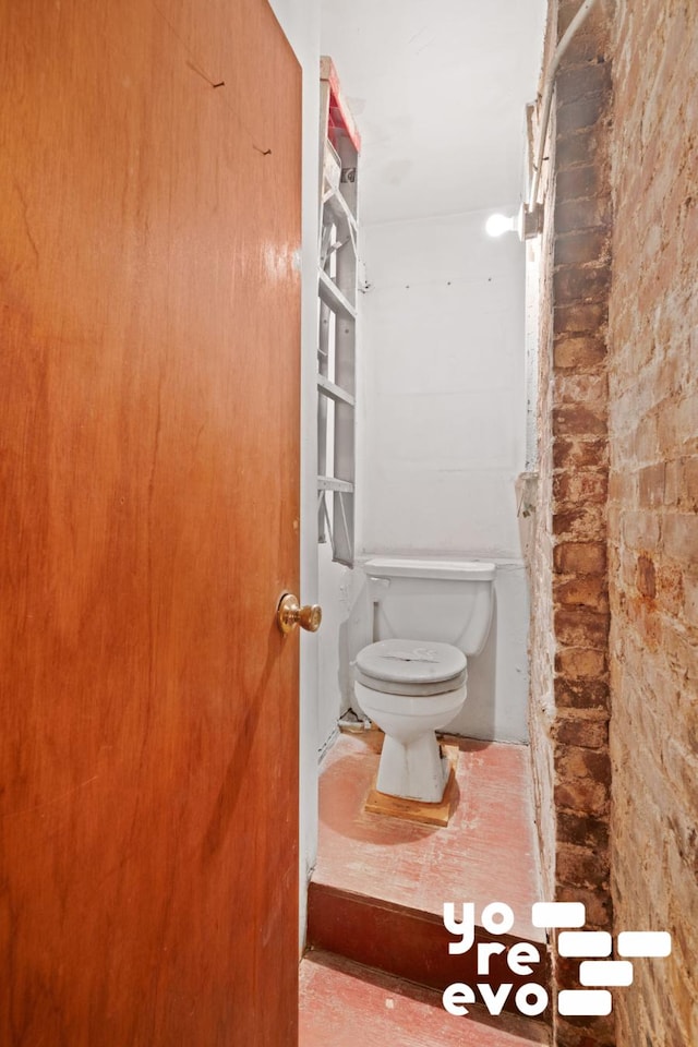 bathroom featuring brick wall and toilet