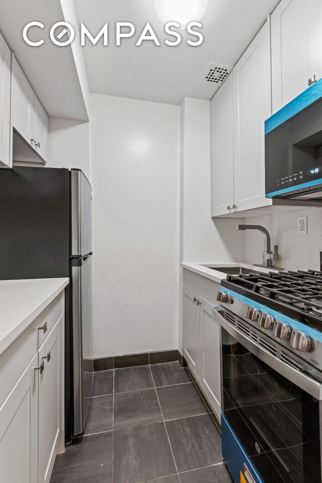 kitchen featuring baseboards, visible vents, stainless steel appliances, white cabinetry, and a sink