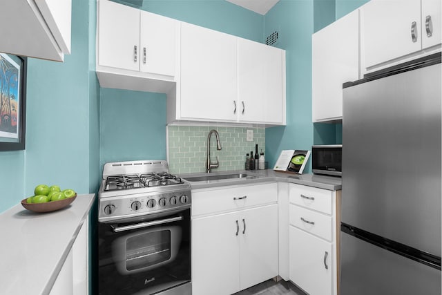 kitchen with appliances with stainless steel finishes, a sink, light countertops, white cabinetry, and backsplash