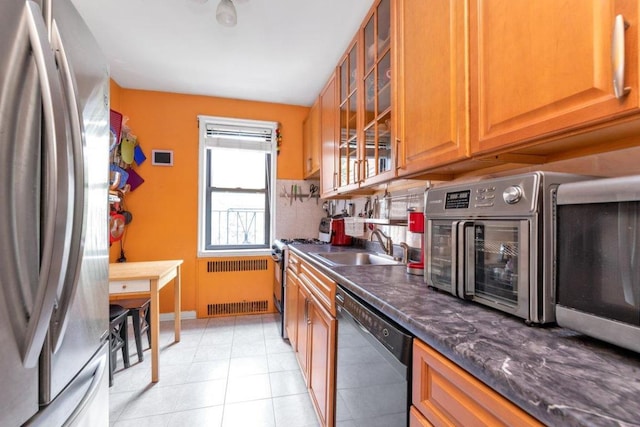 kitchen with radiator, stainless steel appliances, tasteful backsplash, dark stone countertops, and sink