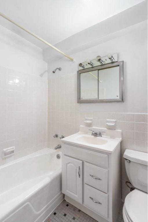 full bathroom featuring tile patterned floors, toilet, tile walls, vanity, and tiled shower / bath combo