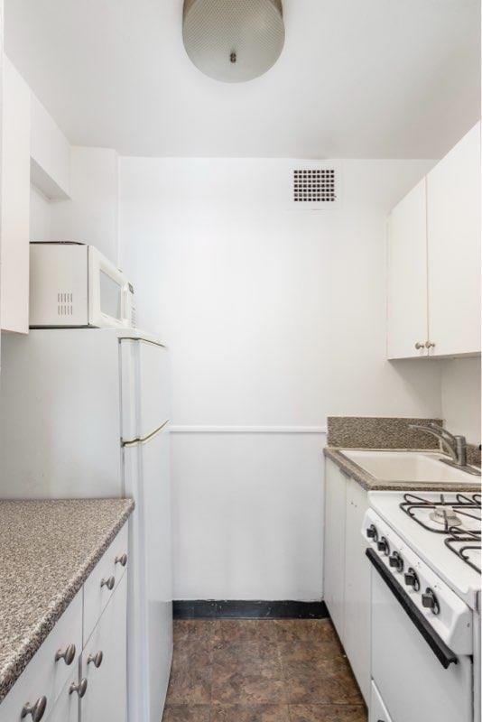 kitchen with white appliances, a sink, visible vents, white cabinetry, and stone finish floor