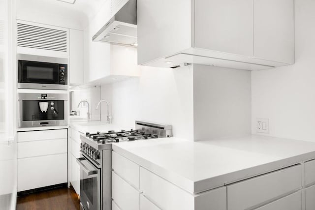 kitchen with dark wood-type flooring, stainless steel appliances, white cabinetry, and wall chimney range hood