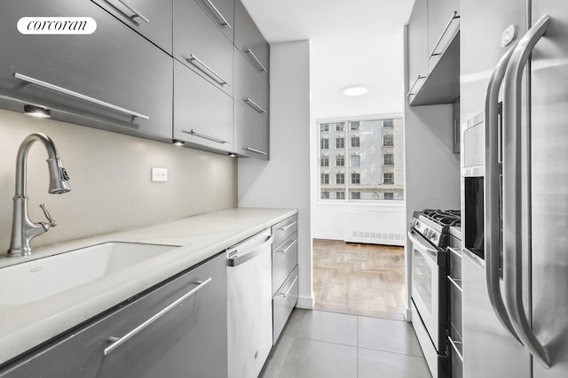 kitchen featuring light tile patterned floors, gray cabinetry, a sink, light countertops, and appliances with stainless steel finishes