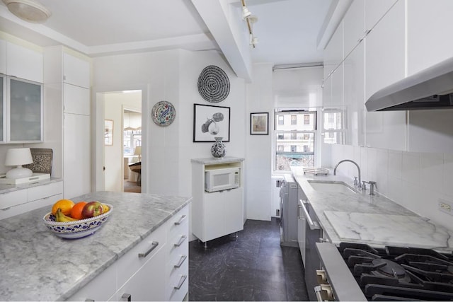 kitchen with white cabinets, white microwave, glass insert cabinets, light stone countertops, and a sink