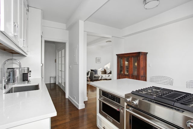 kitchen with stainless steel appliances, a sink, white cabinets, light countertops, and dark wood-style floors