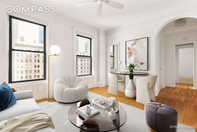 living room with light wood finished floors, arched walkways, baseboards, and a ceiling fan