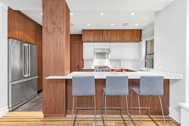 kitchen with high quality fridge, white cabinetry, sink, kitchen peninsula, and stove