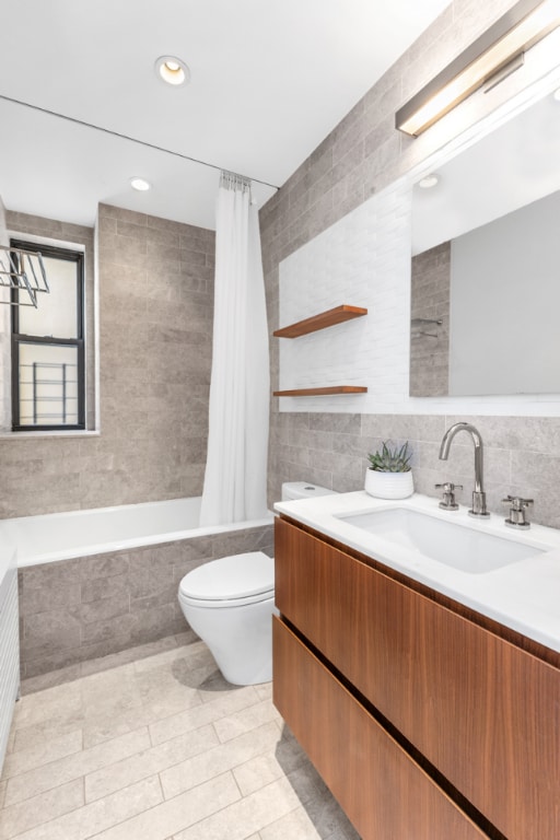 full bathroom featuring tile walls, toilet, vanity, and shower / tub combo