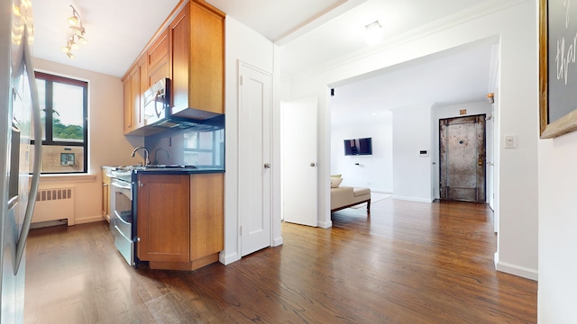 kitchen featuring stainless steel appliances, radiator, dark wood-type flooring, brown cabinets, and baseboards