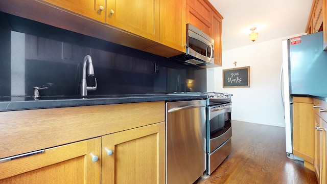 kitchen featuring appliances with stainless steel finishes, dark wood-style floors, brown cabinetry, a sink, and dark countertops