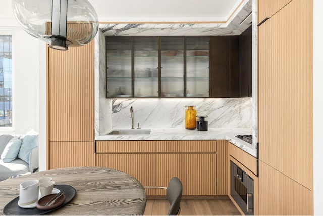 kitchen with oven, a sink, backsplash, wood finished floors, and light countertops