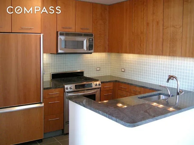 11 E 29th St Unit 28B, New York City, NY 10016 - kitchen with stainless steel appliances, brown cabinetry, a sink, decorative backsplash, and dark stone countertops