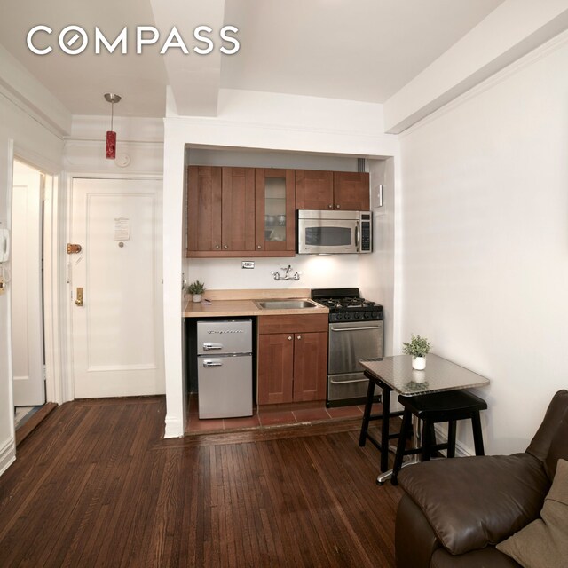 kitchen with glass insert cabinets, dark wood-style flooring, a sink, stainless steel appliances, and brown cabinets