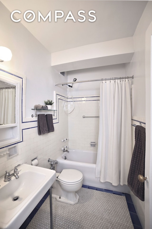 bathroom with a sink, toilet, tile walls, shower / bathtub combination with curtain, and tile patterned floors