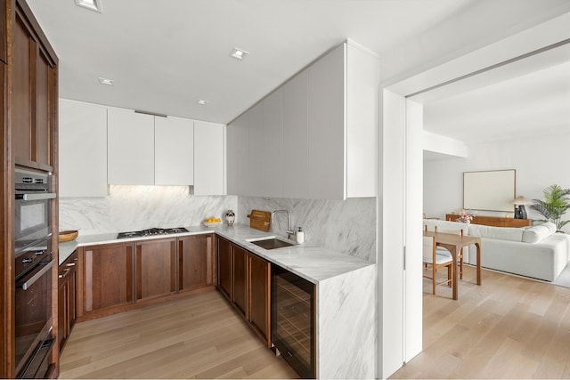 kitchen with beverage cooler, a sink, light wood-style floors, light countertops, and decorative backsplash