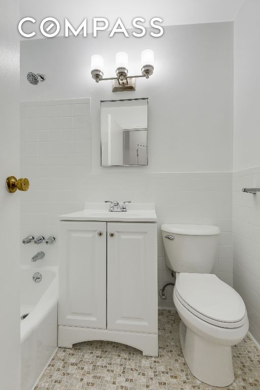 bathroom featuring tile patterned floors, toilet, tile walls, vanity, and a washtub