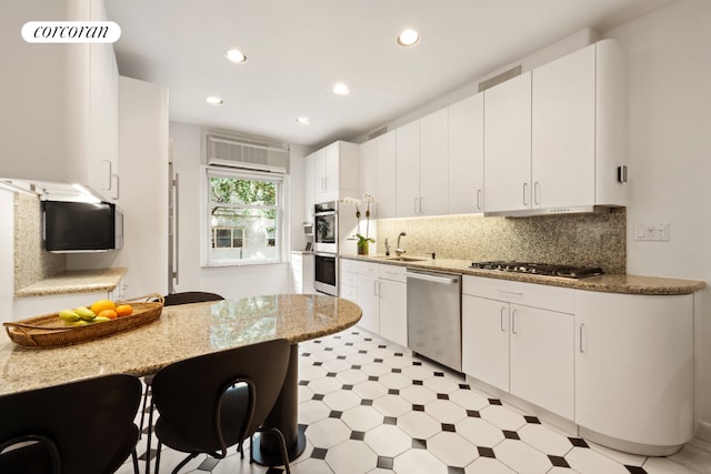 kitchen featuring a kitchen bar, sink, stainless steel appliances, white cabinets, and light stone counters