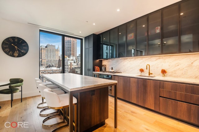 kitchen featuring a kitchen breakfast bar, tasteful backsplash, light hardwood / wood-style floors, expansive windows, and a kitchen island